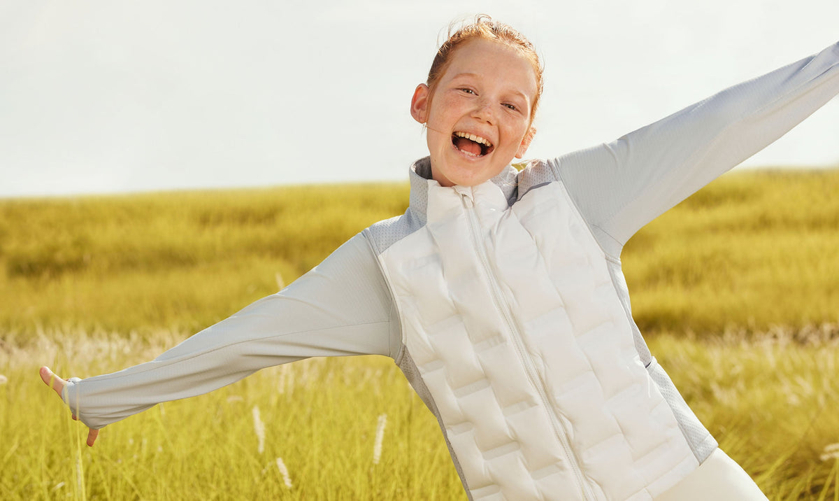 Girl in a white quilted down vest laughing in a sunny grass field