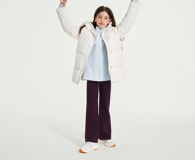 moodytiger child wearing a white winter puffer jacket, light blue top, and dark pants, standing with arms raised against a clean studio background.