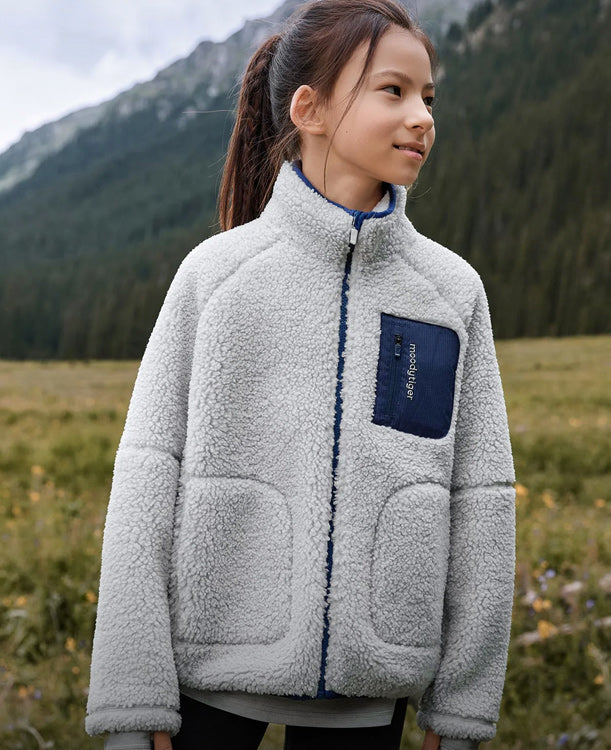 Child wearing a gray fleece jacket with a blue pocket in a mountainous landscape