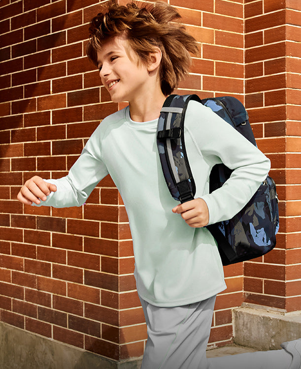 Child with a backpack standing against a brick wall