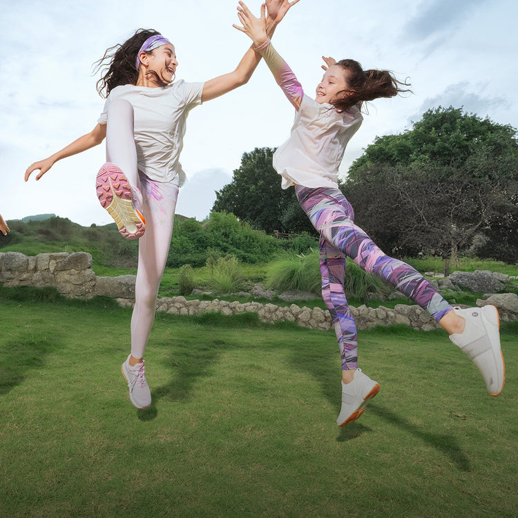 Two young girls wearing colourful leggings by moodytiger jumping in a green outdoor field